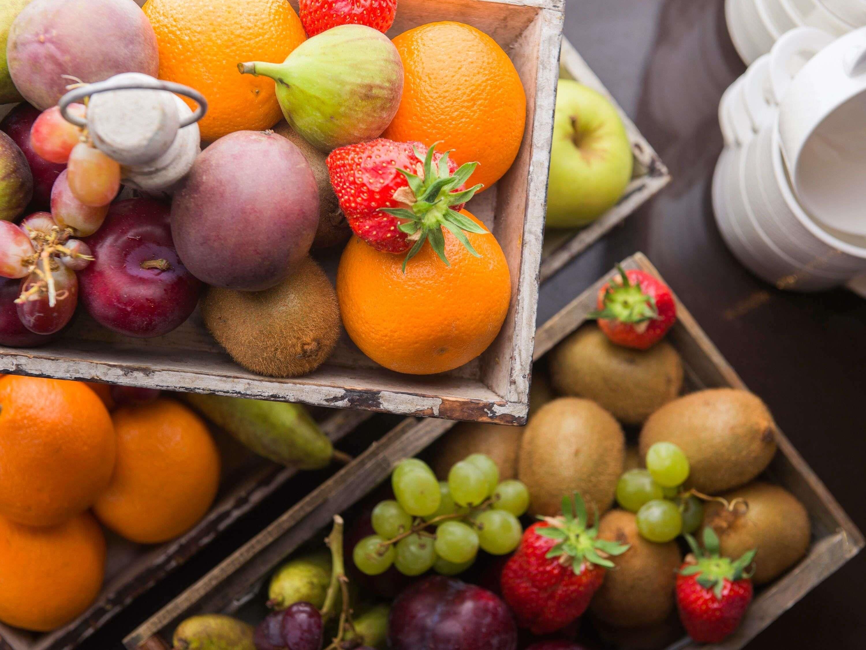 A wooden crate filled with various fruits including apples, oranges, kiwis, and grapes.