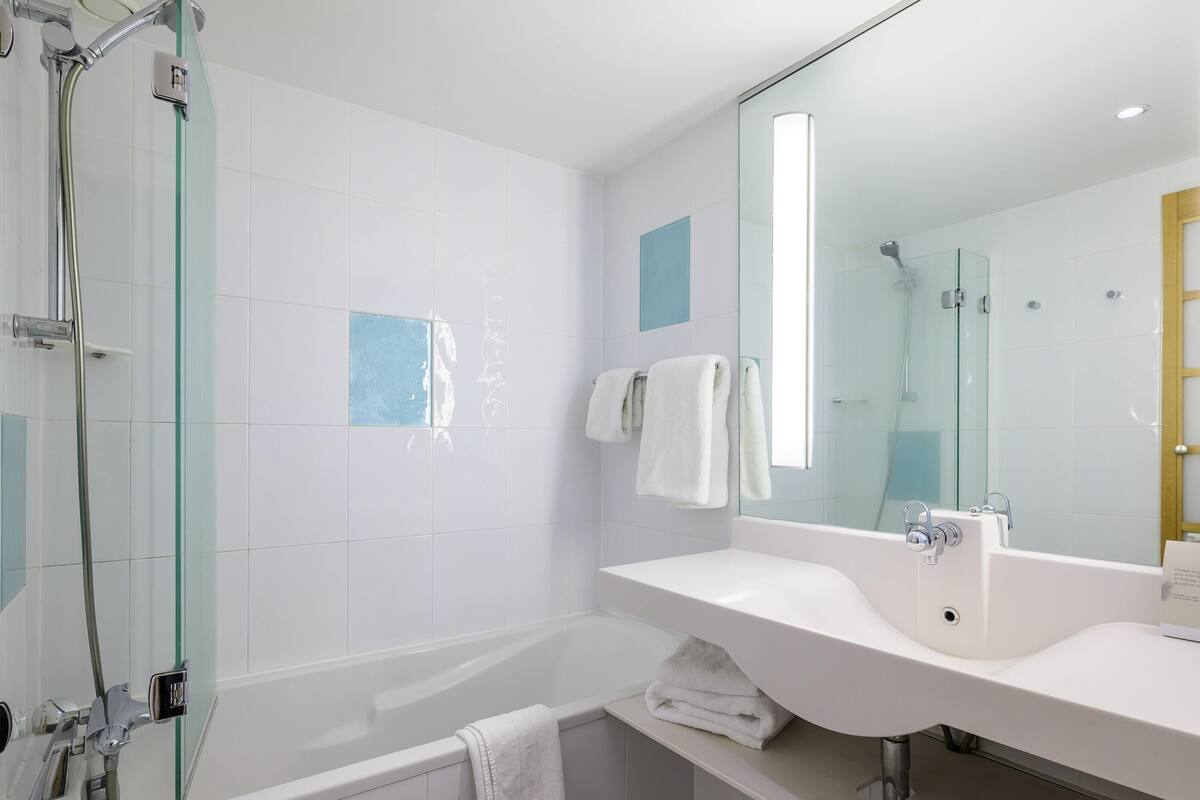 Ein modernes Badezimmer mit einer in Glas eingefassten Dusche, einer weißen Badewanne und einem großen Spiegel über einem weißen Waschbecken.