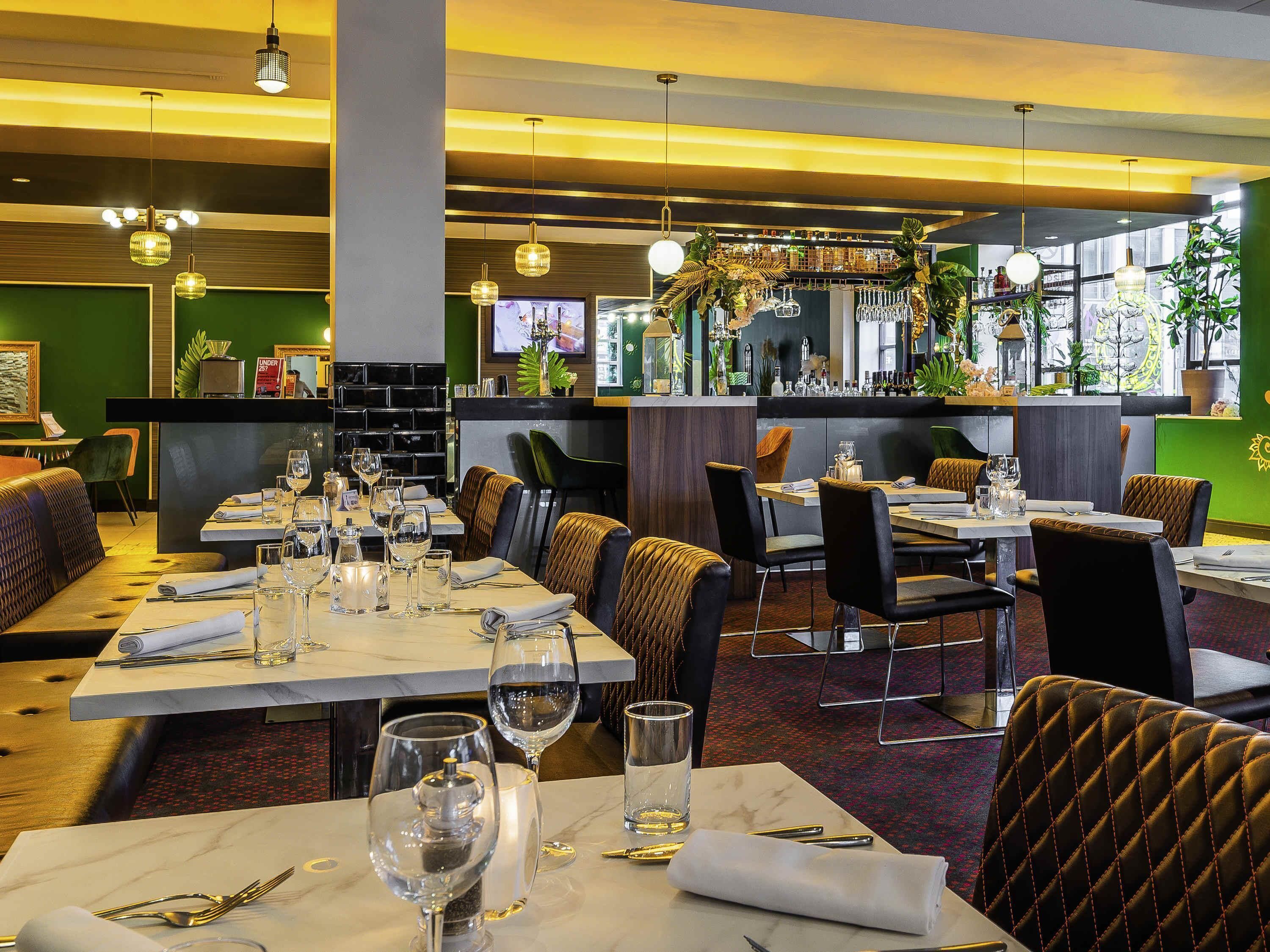 En restaurant med flere spiseborde, stole og hængende pendellamper.