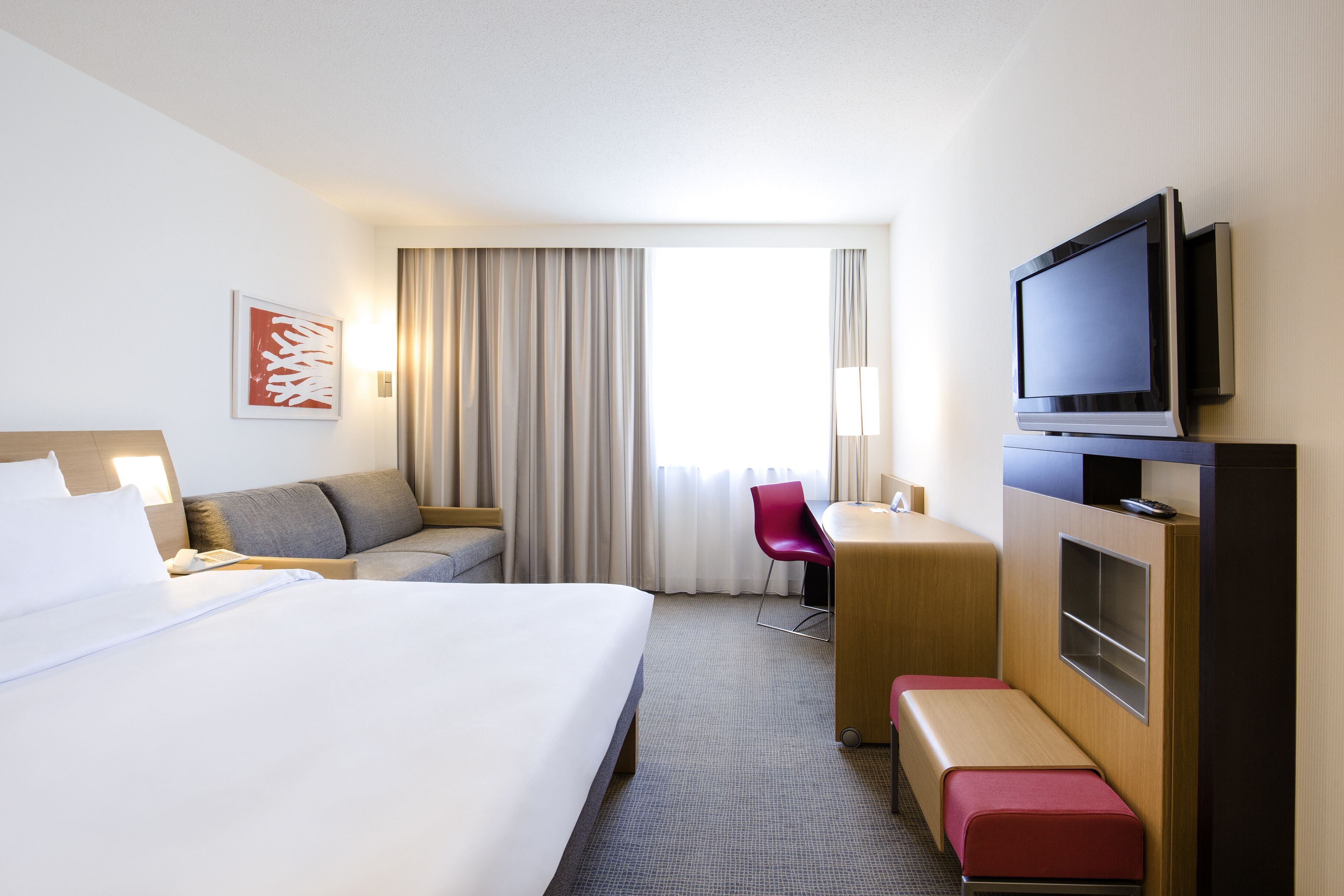 A hotel room with a large bed, a desk with a chair, a television, and a window with curtains.