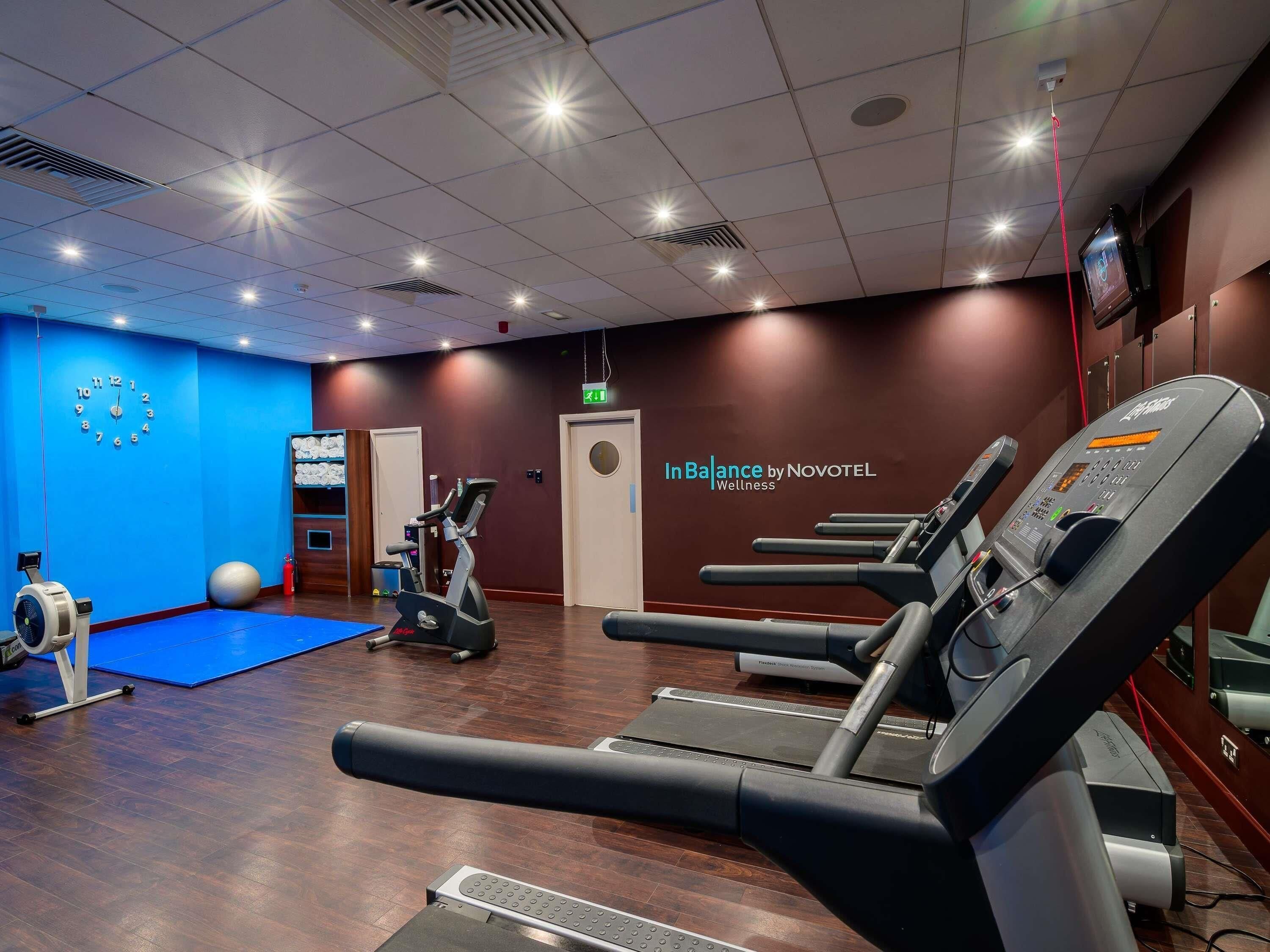 Un gimnasio con cintas de correr, pelotas de ejercicio y un reloj de pared azul.