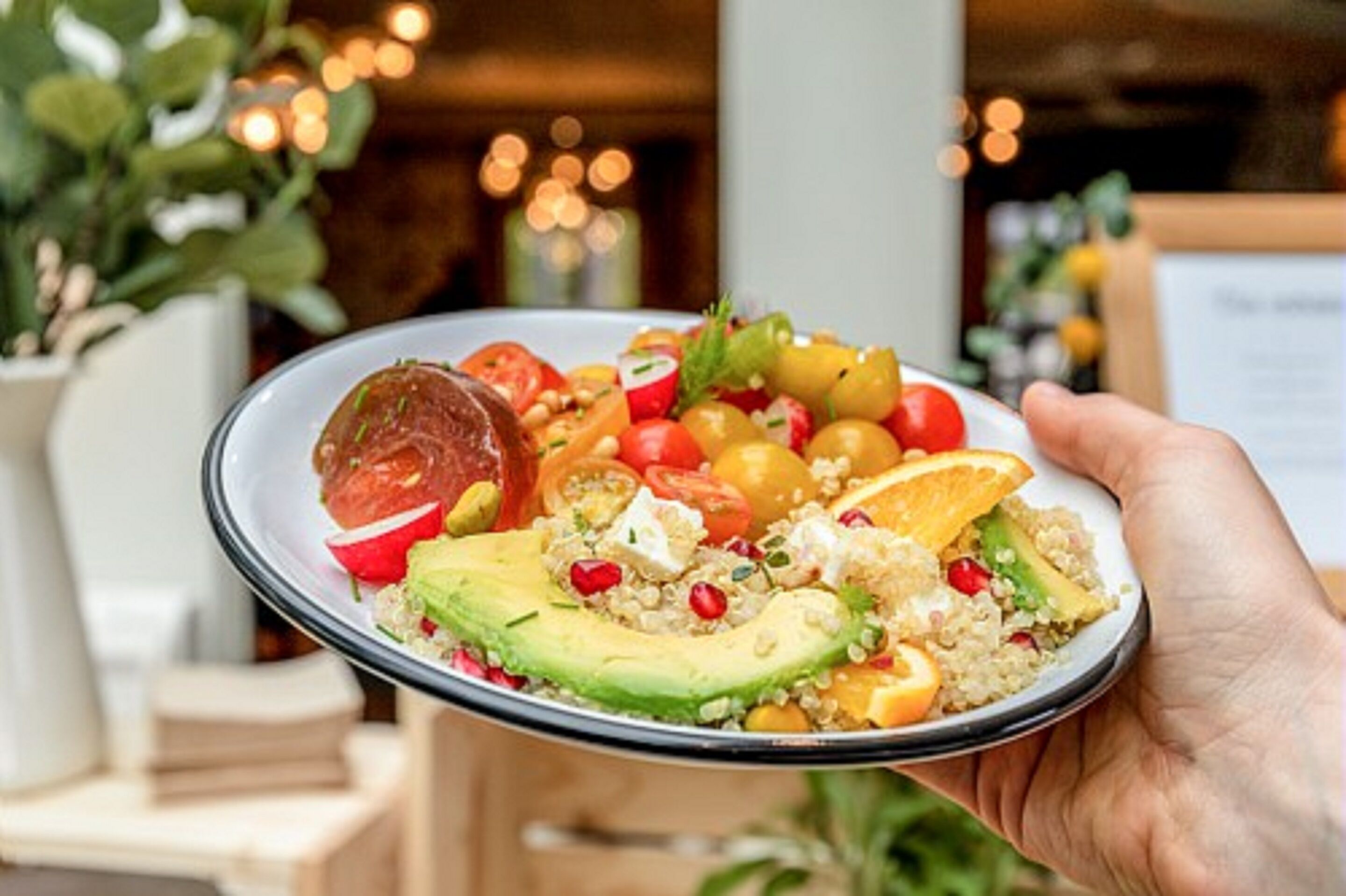 Une personne tenant une assiette contenant une salade de quinoa, de l’avocat, des graines de grenade et des tranches d’orange.
