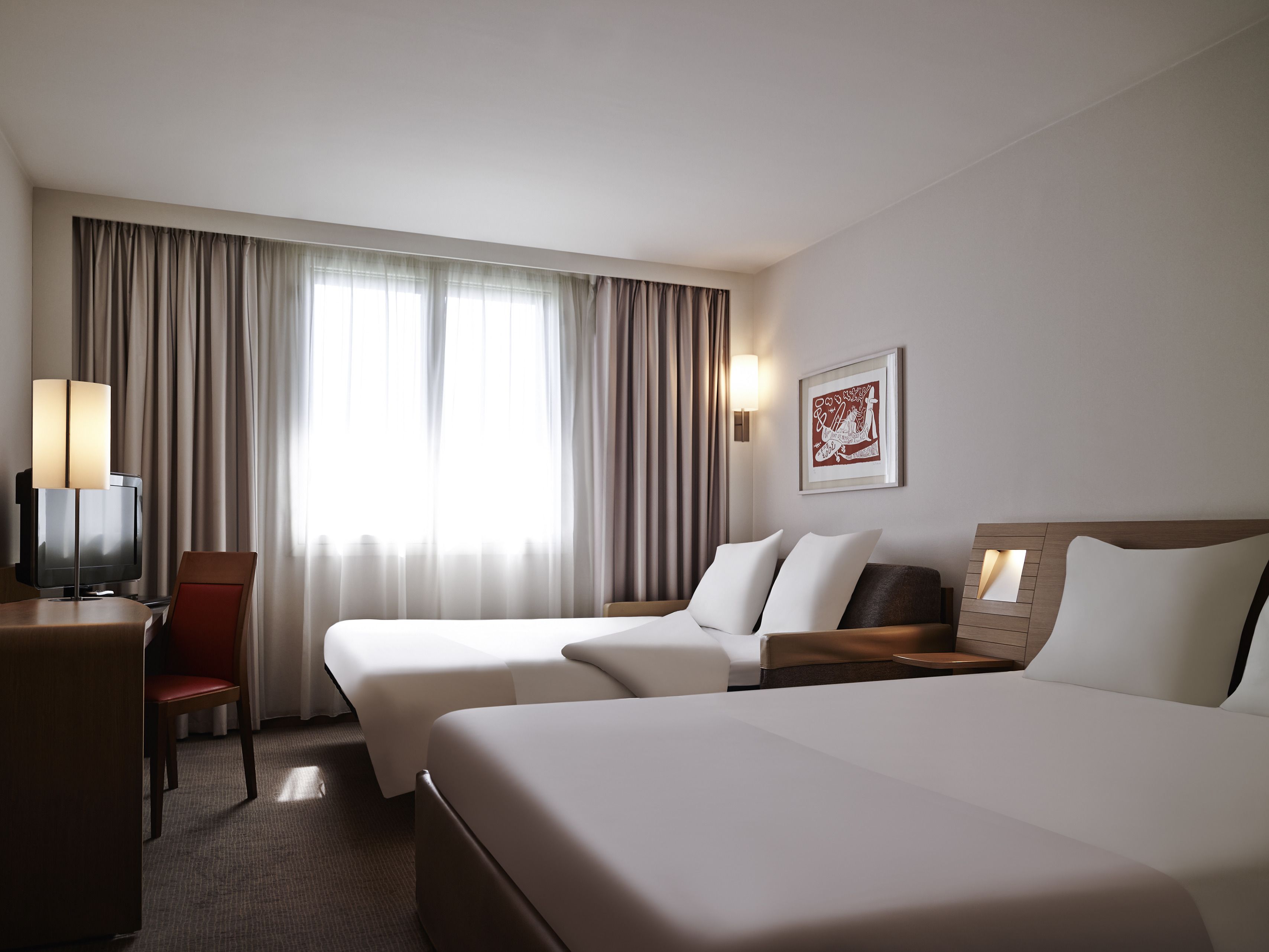 A hotel room with two beds, a desk, a chair, a TV, and a window with curtains.