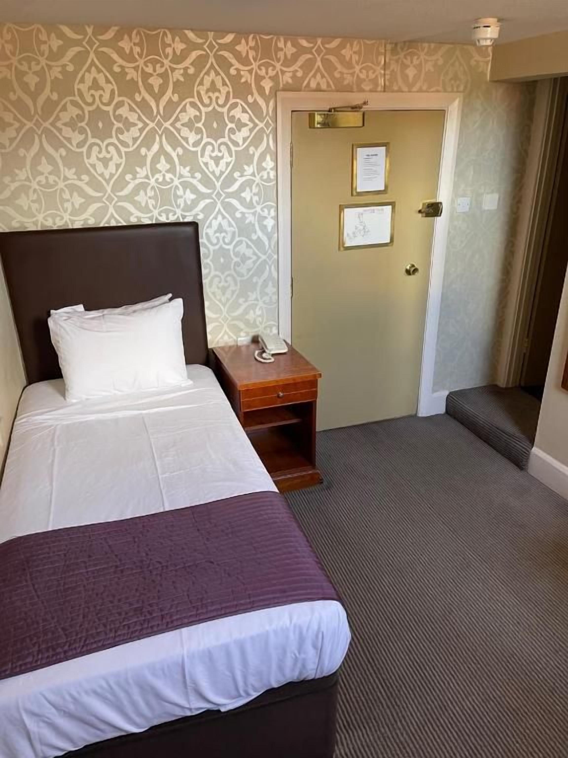 Habitación de hotel con cama, mesita de noche y una puerta con un cartel.