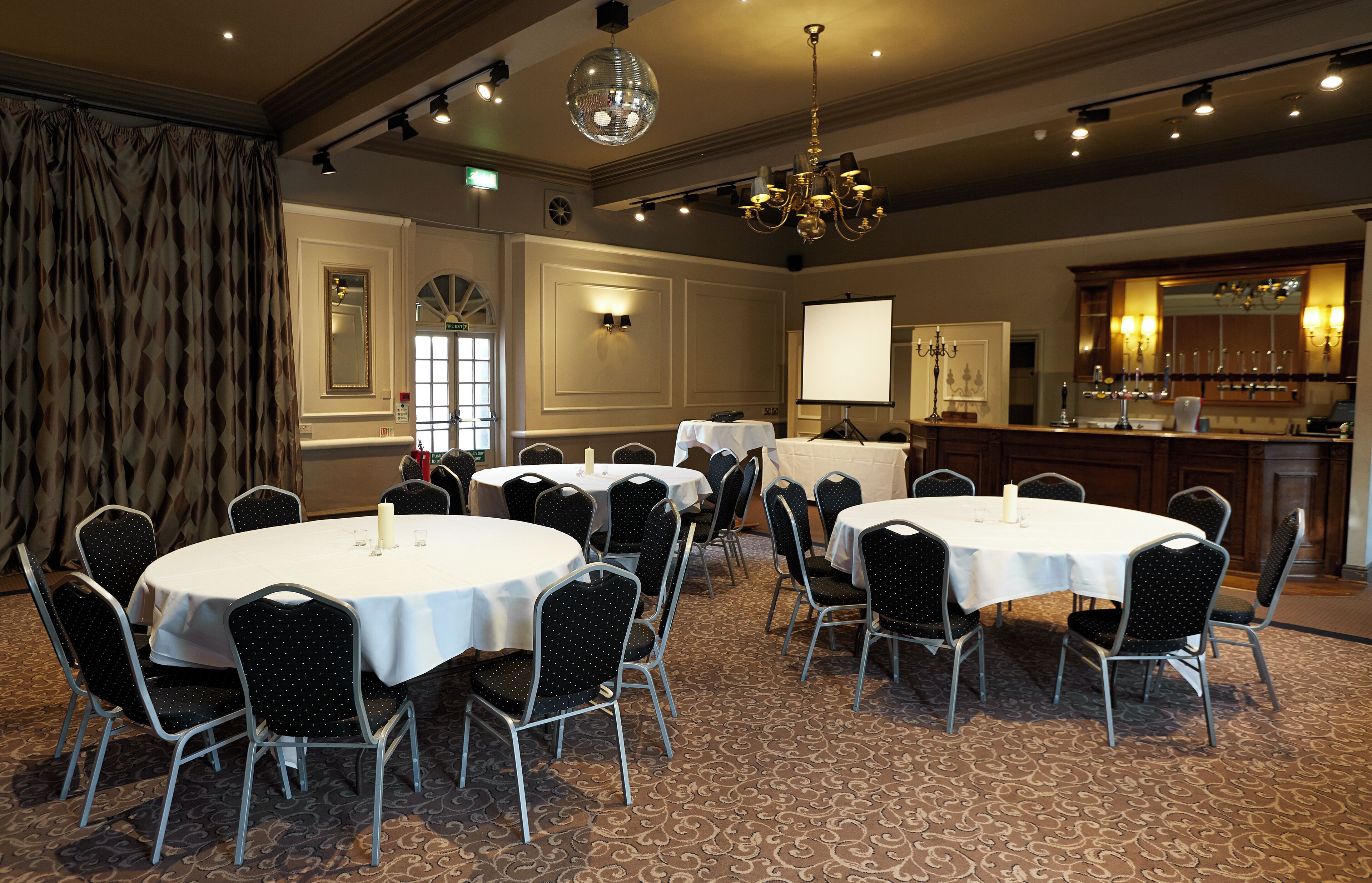 A conference room with round tables and chairs, a bar area, and a large screen.
