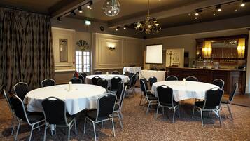 A conference room with round tables and chairs, a bar area, and a large screen.