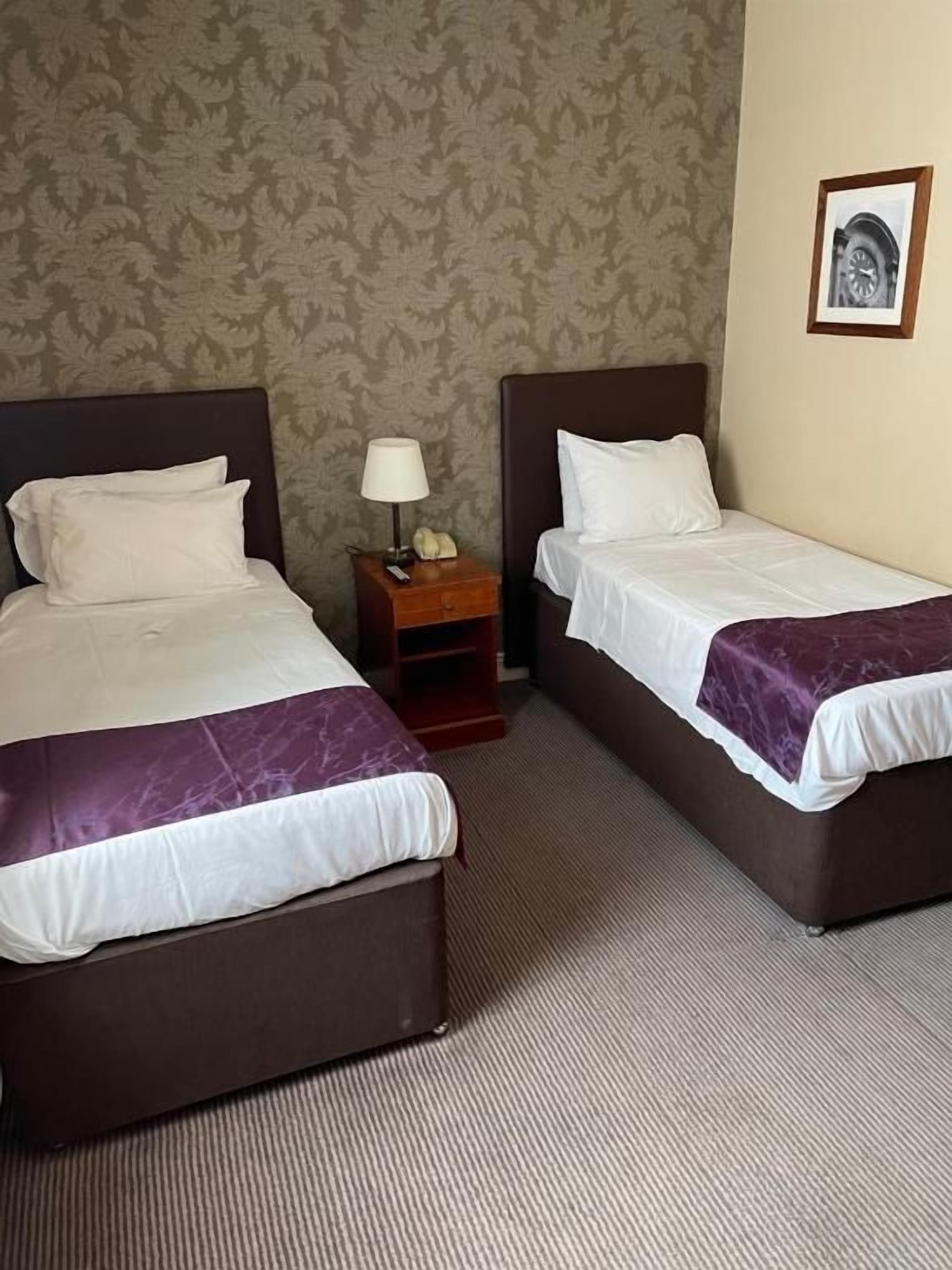 A hotel room with two beds, a nightstand with a lamp, and a framed picture on the wall.