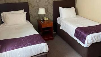 A hotel room with two beds, a nightstand with a lamp, and a framed picture on the wall.