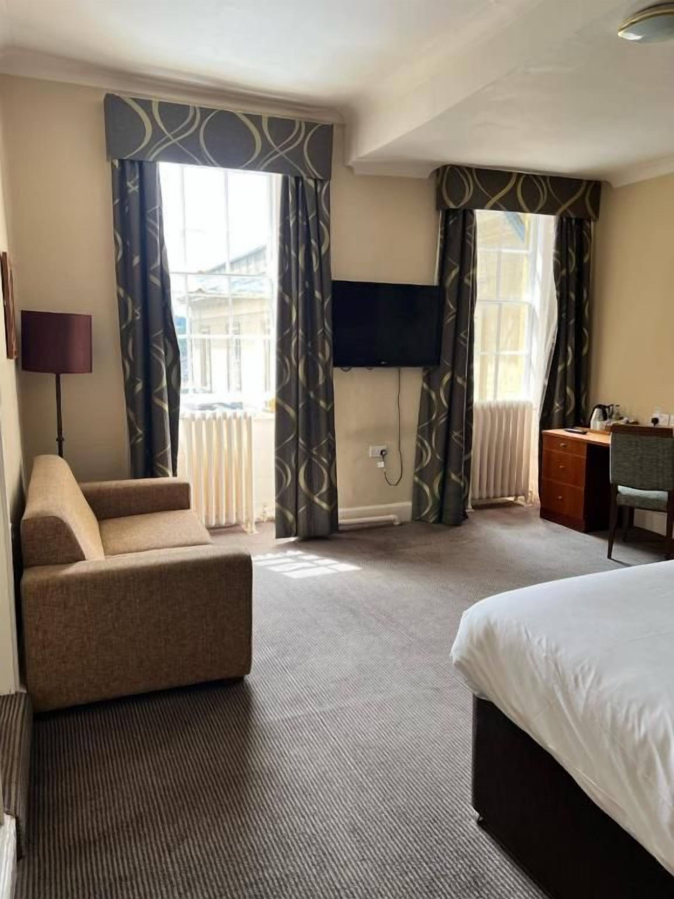 A hotel room with a bed, a sofa, a desk, and a television.