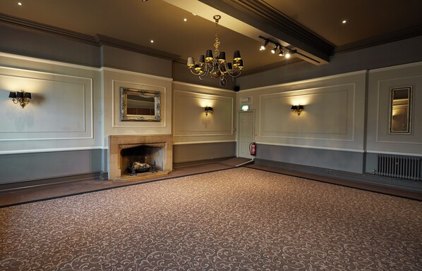 A spacious room with a patterned carpet, a chandelier, wall sconces, a fireplace, and a mirror. - The Manor Hotel by Greene King Inns (Yeovil)
