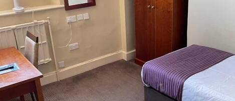 A hotel room with a bed, a desk, a wardrobe, a radiator, and a mirror.
