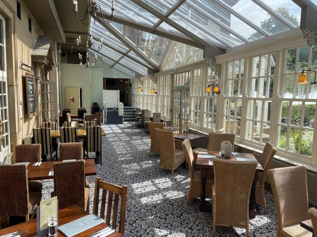 A restaurant with a glass ceiling, wicker furniture, and a patterned carpet.