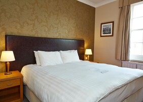Habitación de hotel con una cama grande, dos lámparas de noche, un cuadro en la pared y una ventana con cortinas.