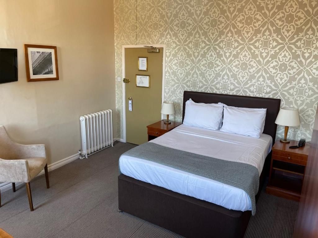 A hotel room with a bed, bedside tables, a chair, a radiator, and a patterned wallpaper.