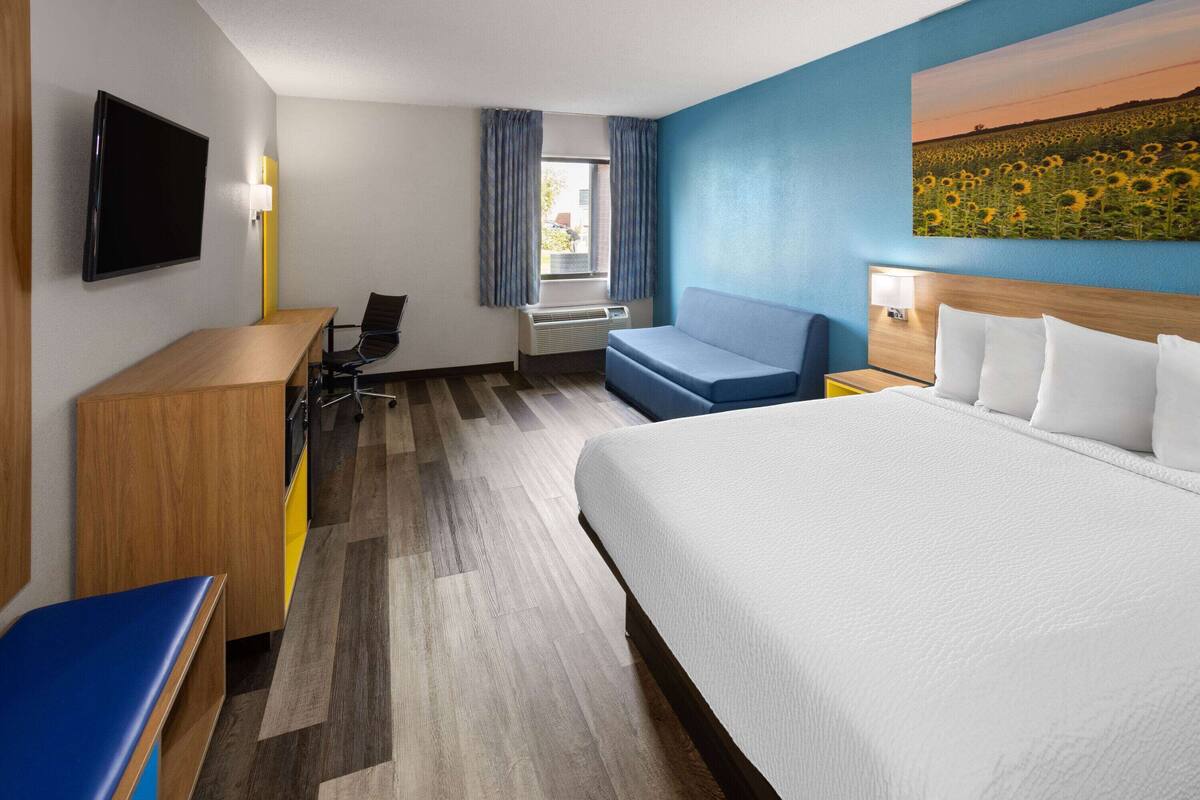 Habitación de hotel con cama, escritorio, silla, televisión y ventana con cortinas.