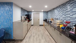 A modern kitchen with a wooden floor, light-colored cabinets, and a blue patterned wall. - Days Inn & Suites by Wyndham Northwest Indianapolis (Indianapolis)