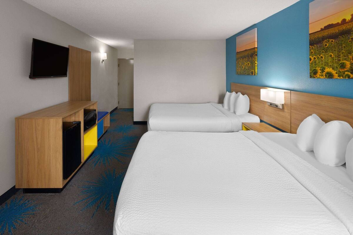 Habitación de hotel con dos camas, televisión, escritorio y un cuadro en la pared.