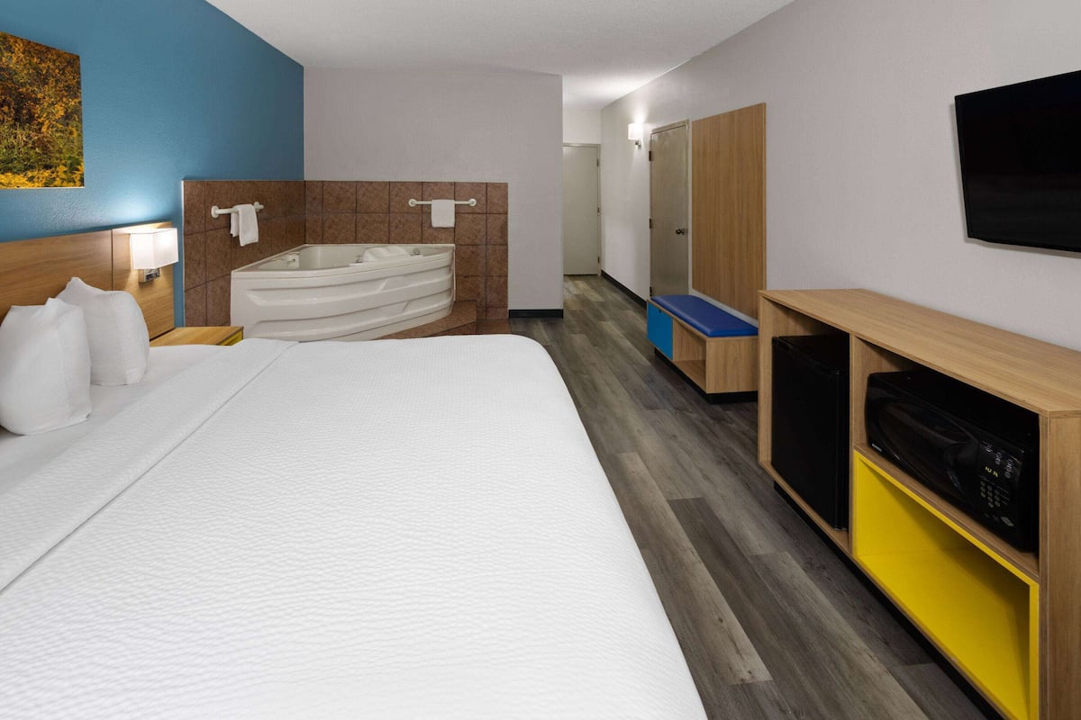 Una habitación de hotel con una cama grande, una bañera, un televisor y un armario de madera.