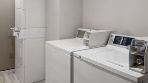 A laundry area with two white washing machines and a control panel. - Days Inn & Suites by Wyndham Northwest Indianapolis (Indianapolis)