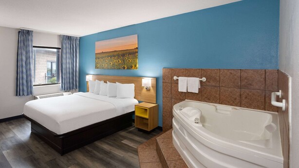 A hotel room with a large bed, a bathroom with a bathtub, and a painting on the wall. - Days Inn & Suites by Wyndham Northwest Indianapolis (Indianapolis)