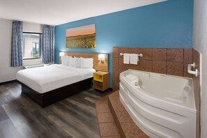 A hotel room with a large bed, a bathroom with a bathtub, and a painting on the wall. - Days Inn & Suites by Wyndham Northwest Indianapolis (Indianapolis)