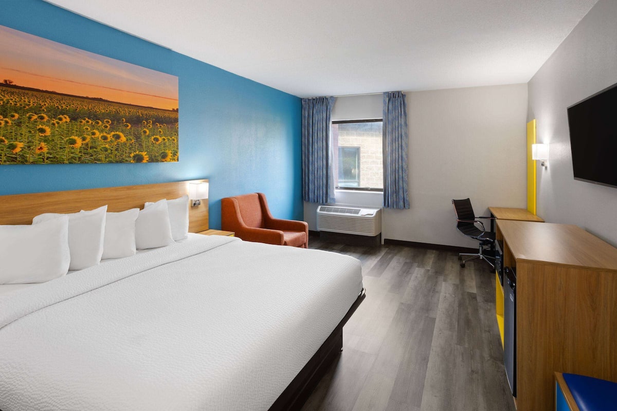 Habitación de hotel con una cama grande, un escritorio, una silla y un cuadro de girasoles en la pared.