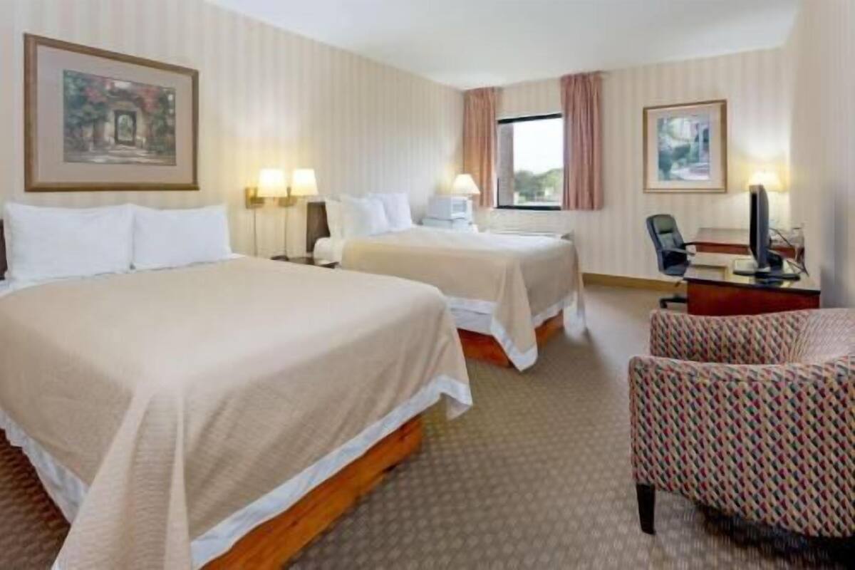 Una habitación de hotel con dos camas, un escritorio, una silla y dos cuadros en las paredes.