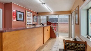 Ein Empfangsbereich mit Holztresen, gerahmten Bildern, einem roten Schild und Blick auf ein Backsteinhaus durch eine Glastür.