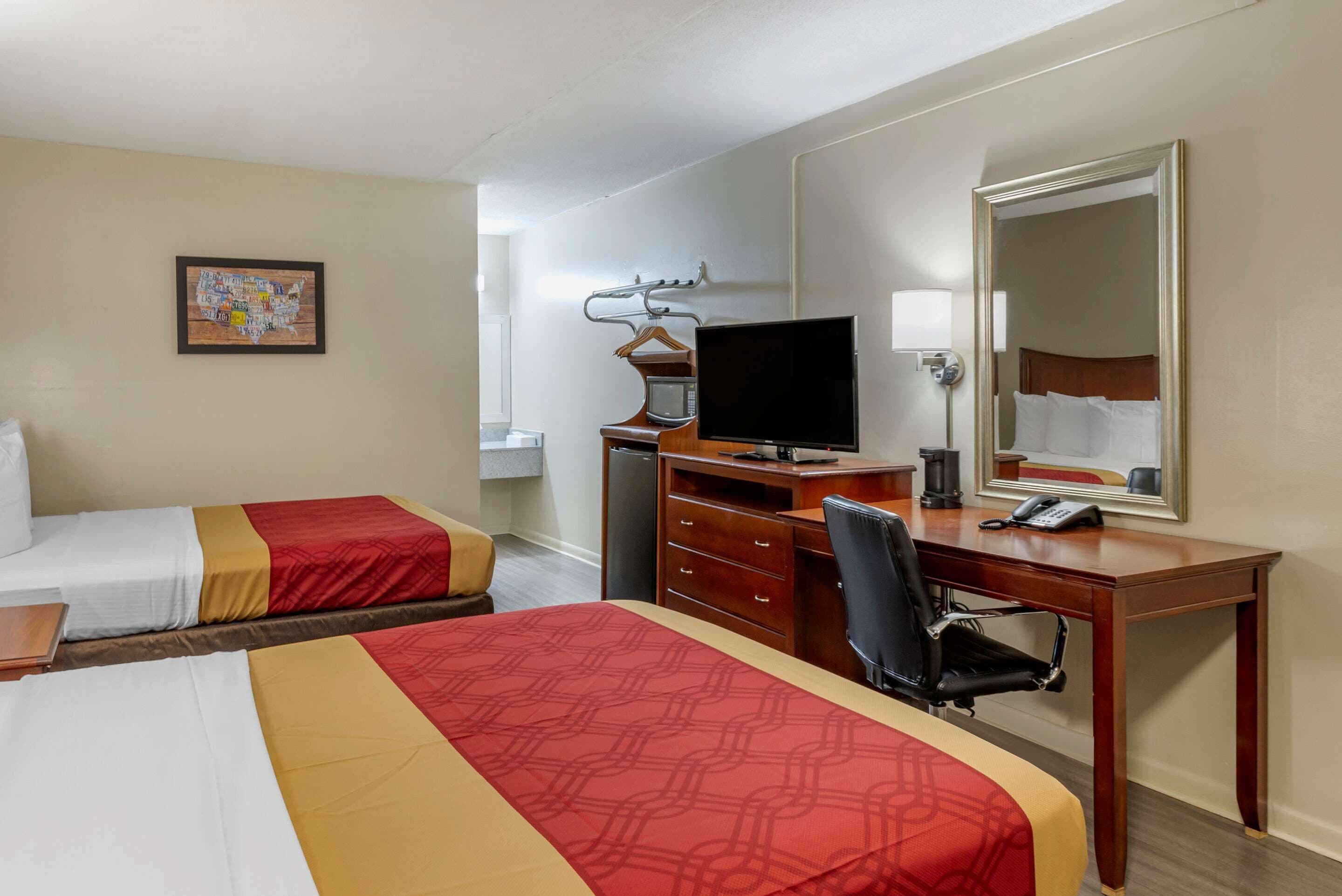 A hotel room with two beds, a desk with a computer, a chair, a dresser, a mirror, and a wall-mounted TV.