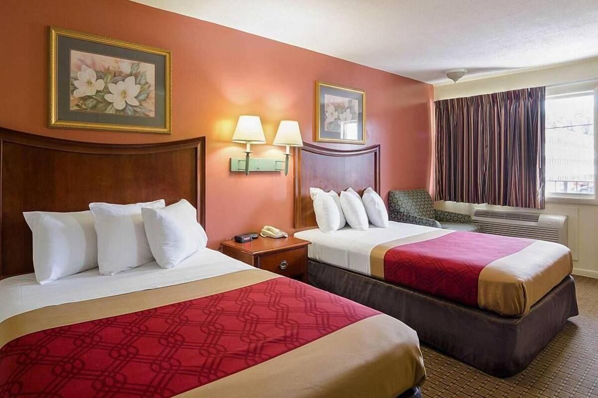 Une chambre d’hôtel avec deux lits, une table de chevet avec un téléphone, des lampes fixées au mur et une fenêtre avec des rideaux.
