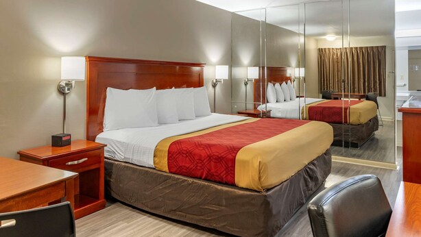 Ein Hotelzimmer mit einem großen Bett, einem Schreibtisch, einem Sessel, einem Nachttisch, einer Lampe und einem Spiegel.