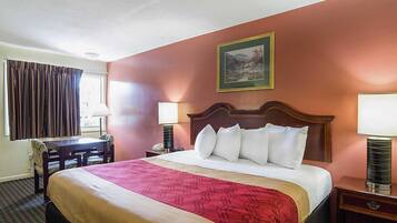 Hotelkamer met een groot bed, een bureau, twee lampen, een schilderij aan de muur en een raam met gordijnen.