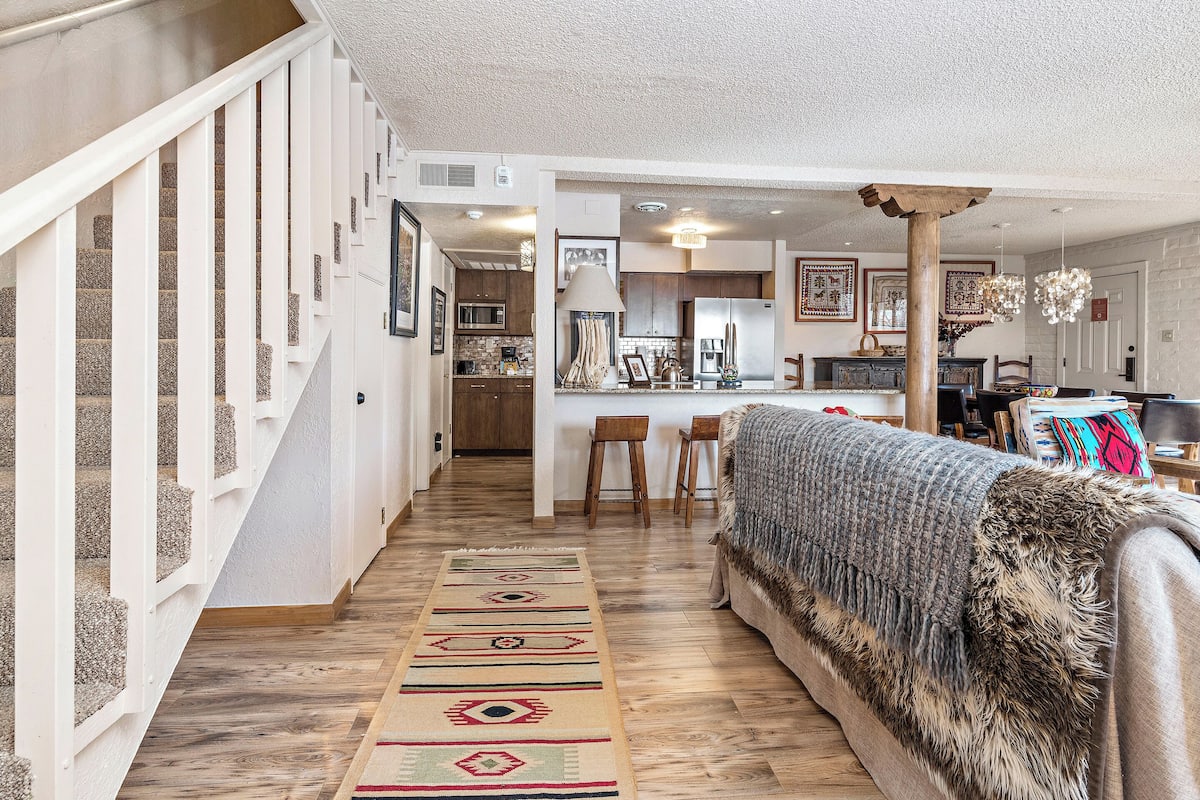 A spacious living area with a staircase, a kitchen in the background, and a cozy seating area with a fur throw.