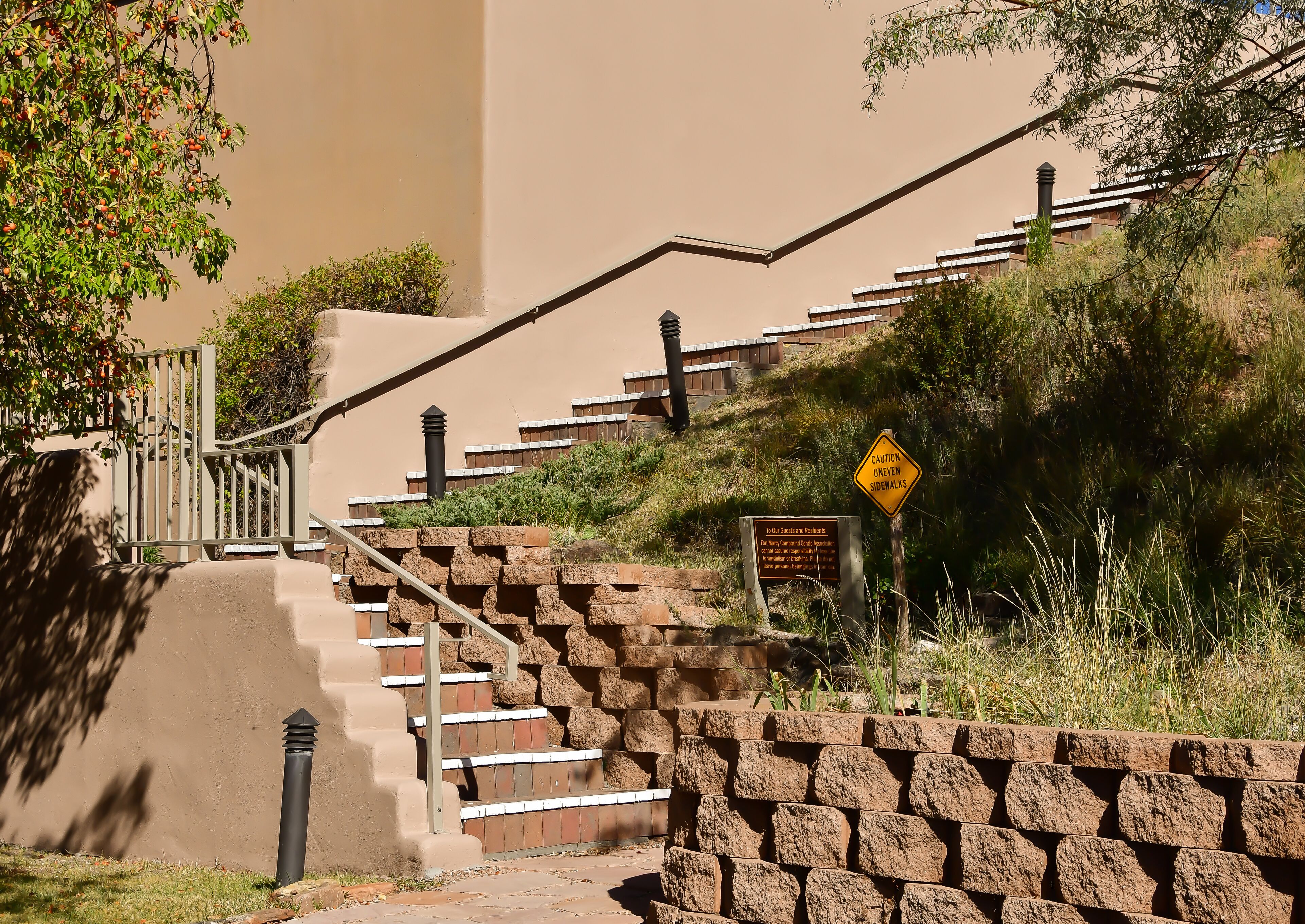 A staircase with stone railings and a caution sign for uneven sidewalks.