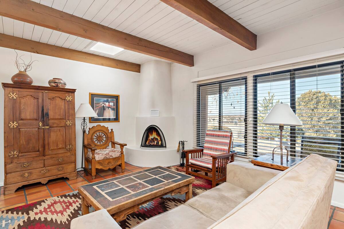 A cozy living room with a fireplace, wooden furniture, and large windows.