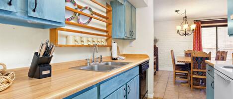 A kitchen with blue cabinets, a wooden countertop, a sink, and a dining area with a table and chairs.