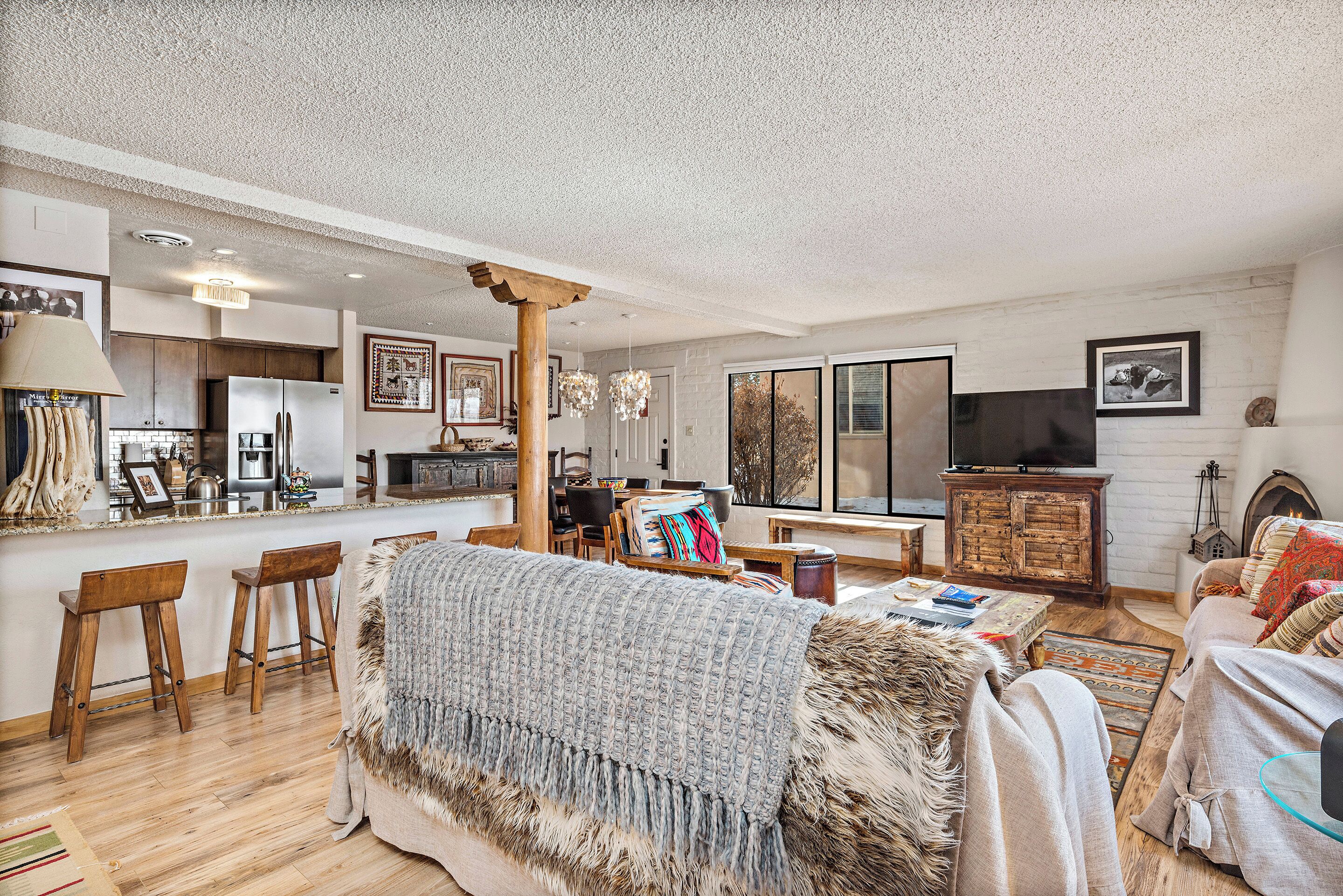 A spacious living room with a large sofa, a coffee table, and a fireplace. There is a kitchen area with a refrigerator and a dining table.