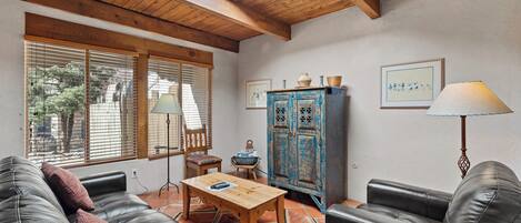 Ein gemütliches Wohnzimmer mit Holzboden, einem schwarzen Ledersofa, einem Holztisch und einem blauen Schrank mit Dekorationselementen.