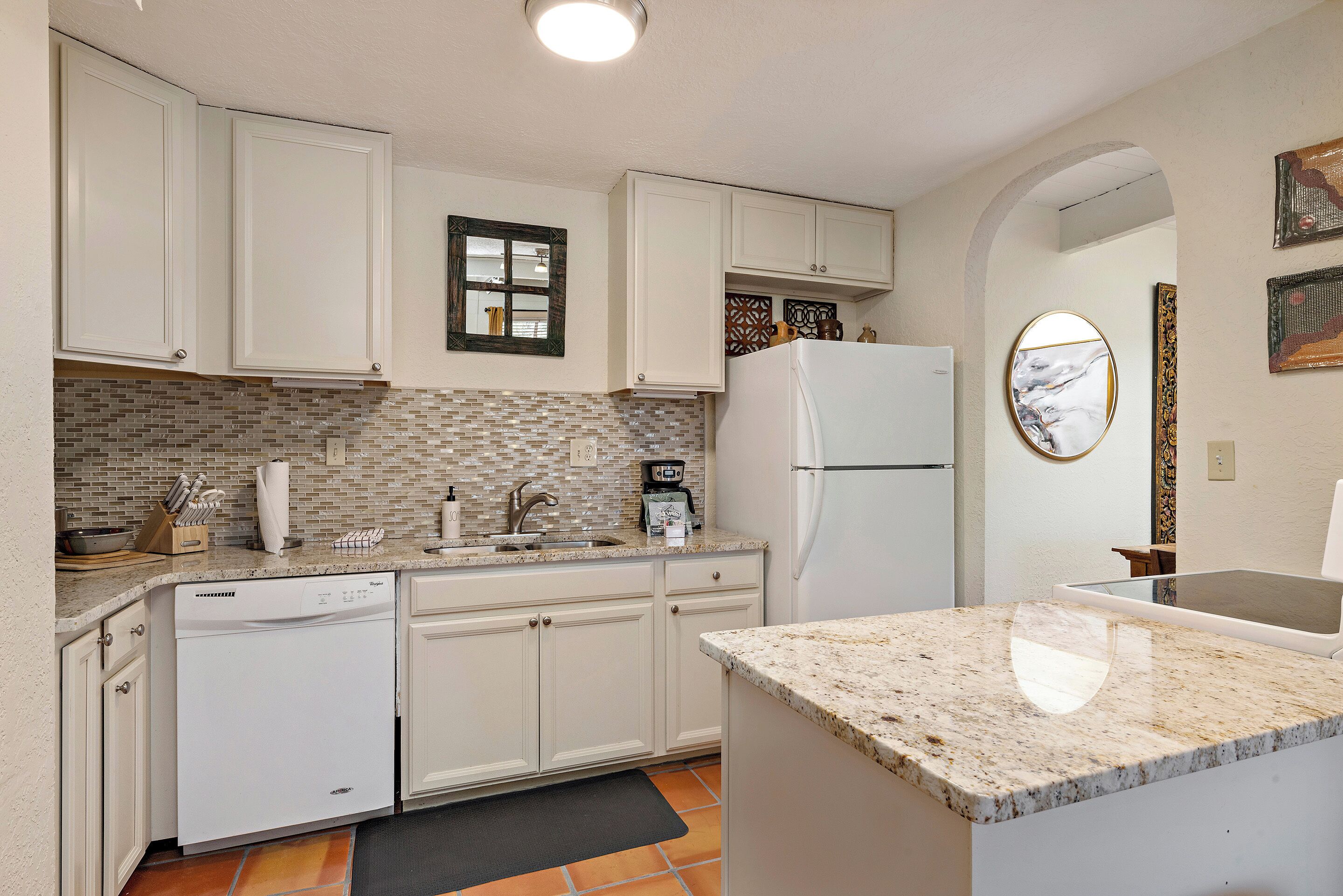 A kitchen with white cabinets, a dishwasher, a refrigerator, and a tiled backsplash.