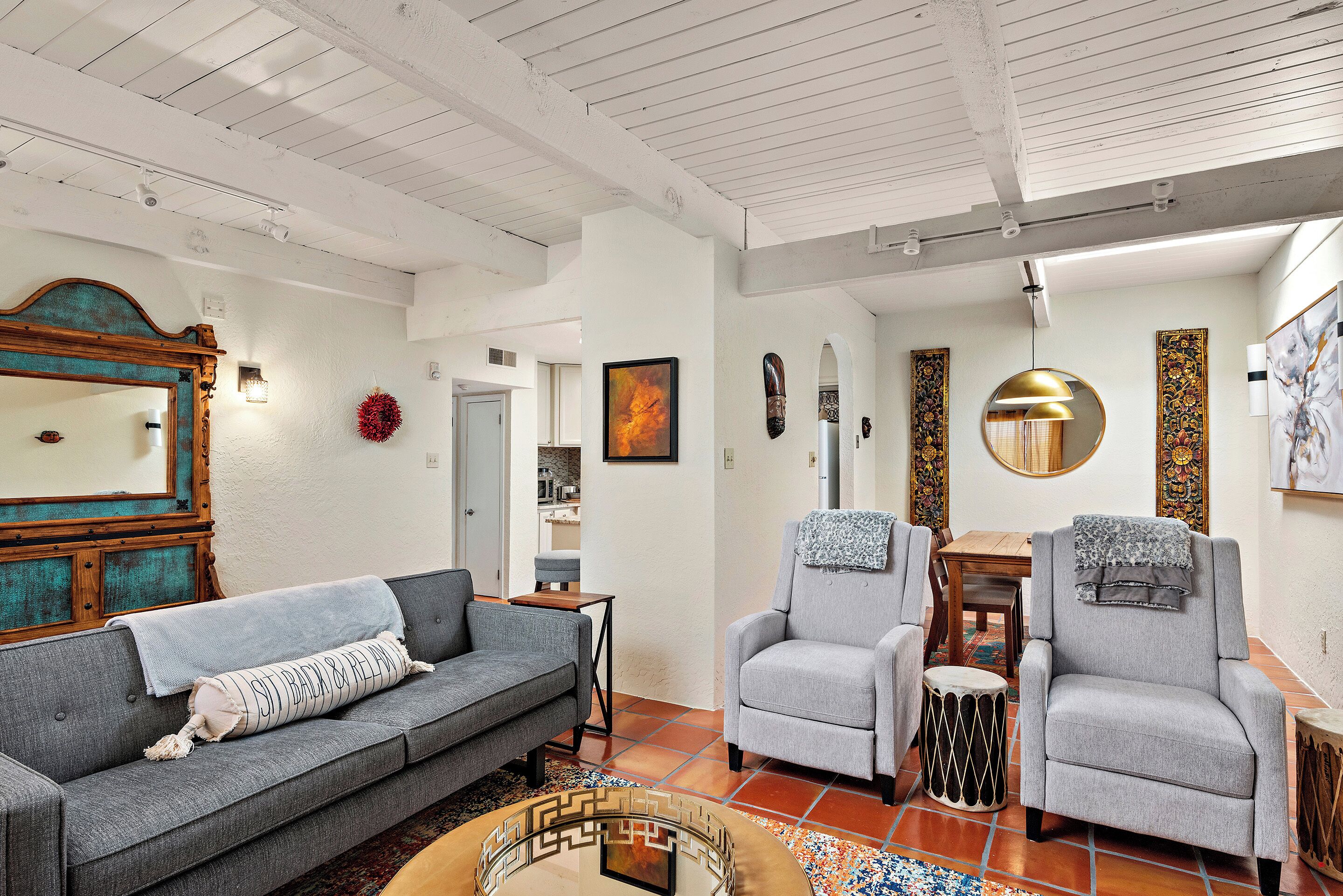 A living room with a grey sofa, two armchairs, a coffee table, and a dining area with a wooden table and chairs.