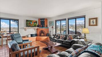 A spacious living room with a fireplace, large windows, and a view of the mountains.