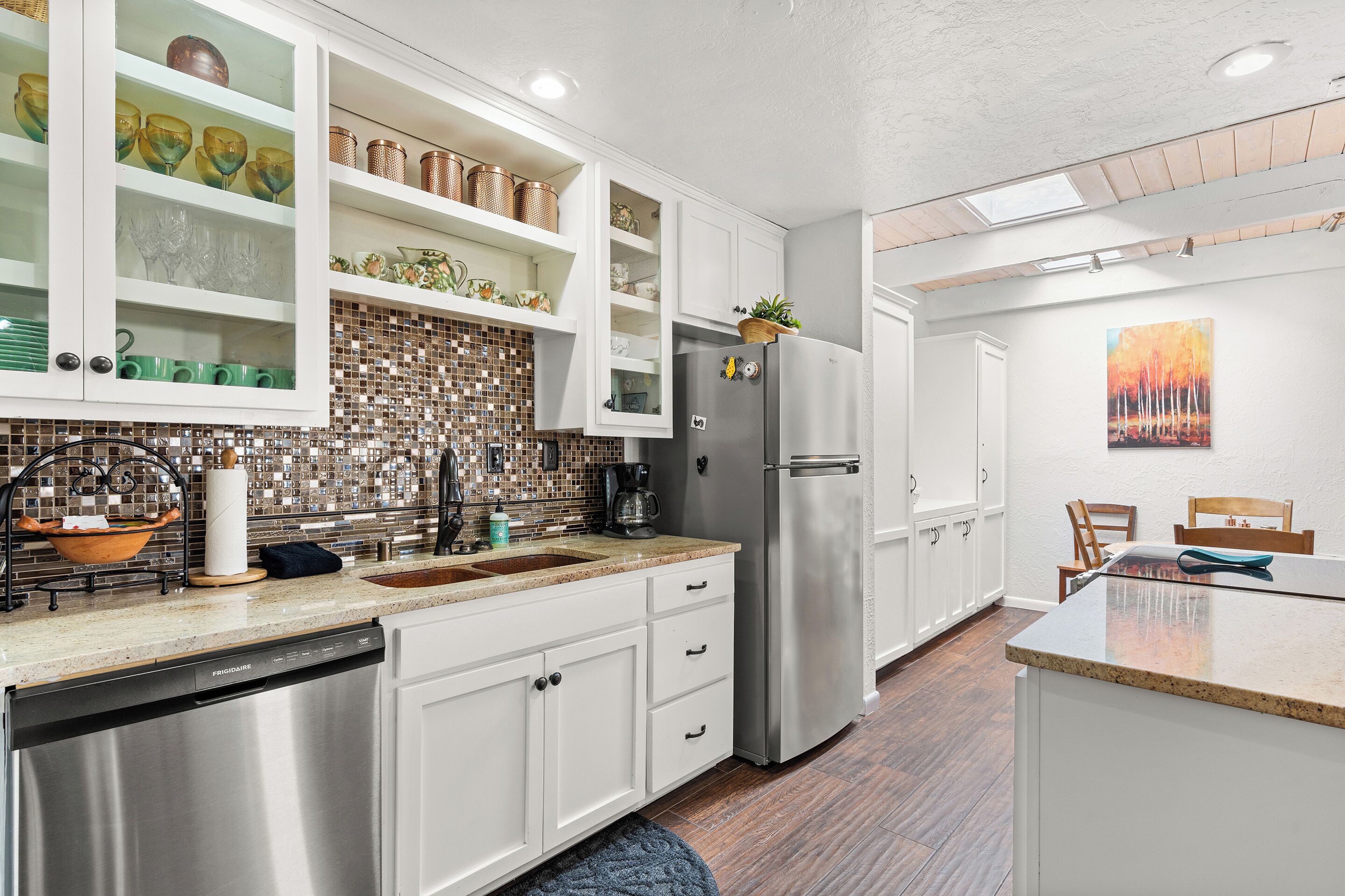 A modern kitchen with white cabinetry, a stainless steel refrigerator, and a mosaic backsplash.