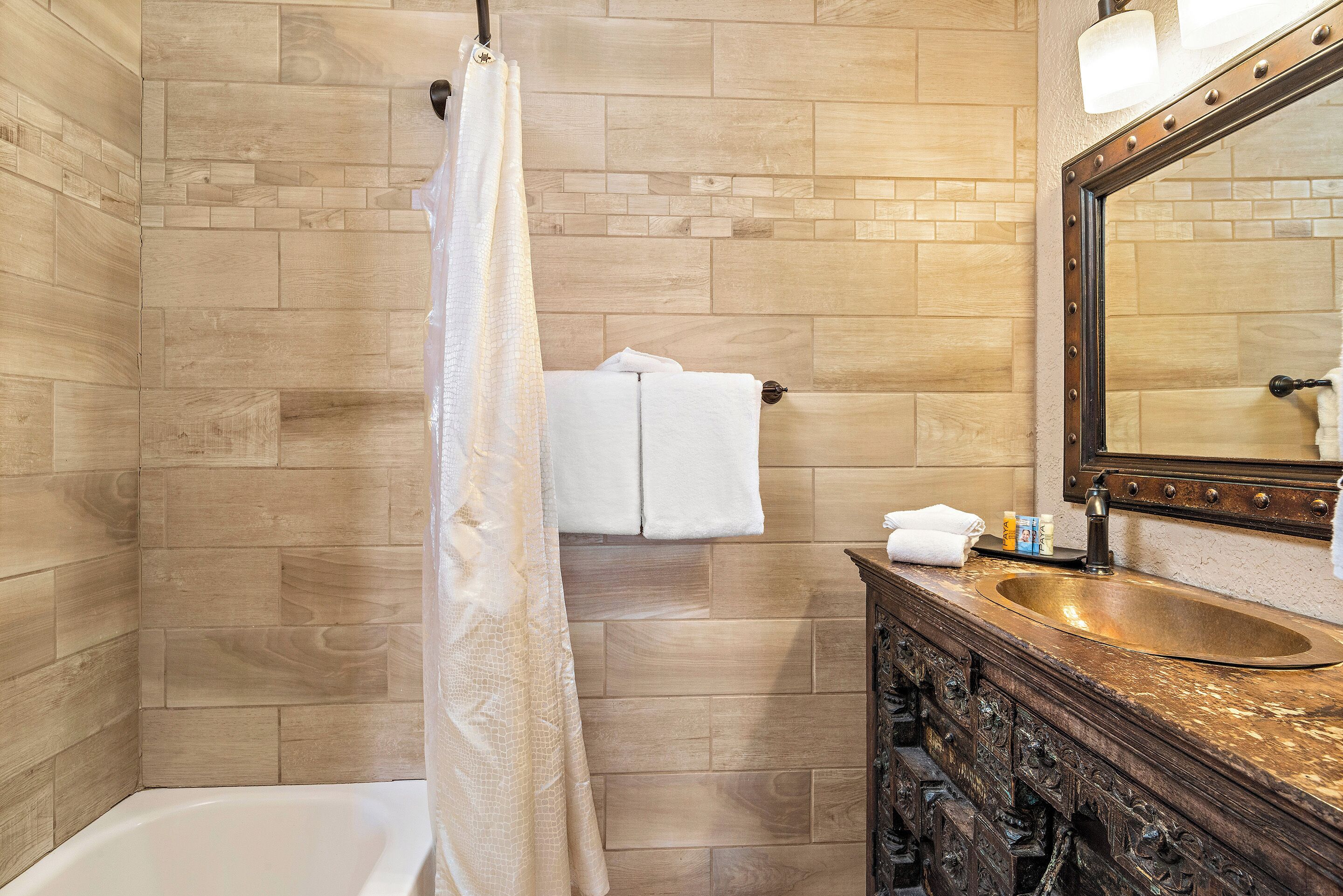 A bathroom with a wooden tiled wall, a white bathtub, a wooden vanity with a sink, and a mirror.