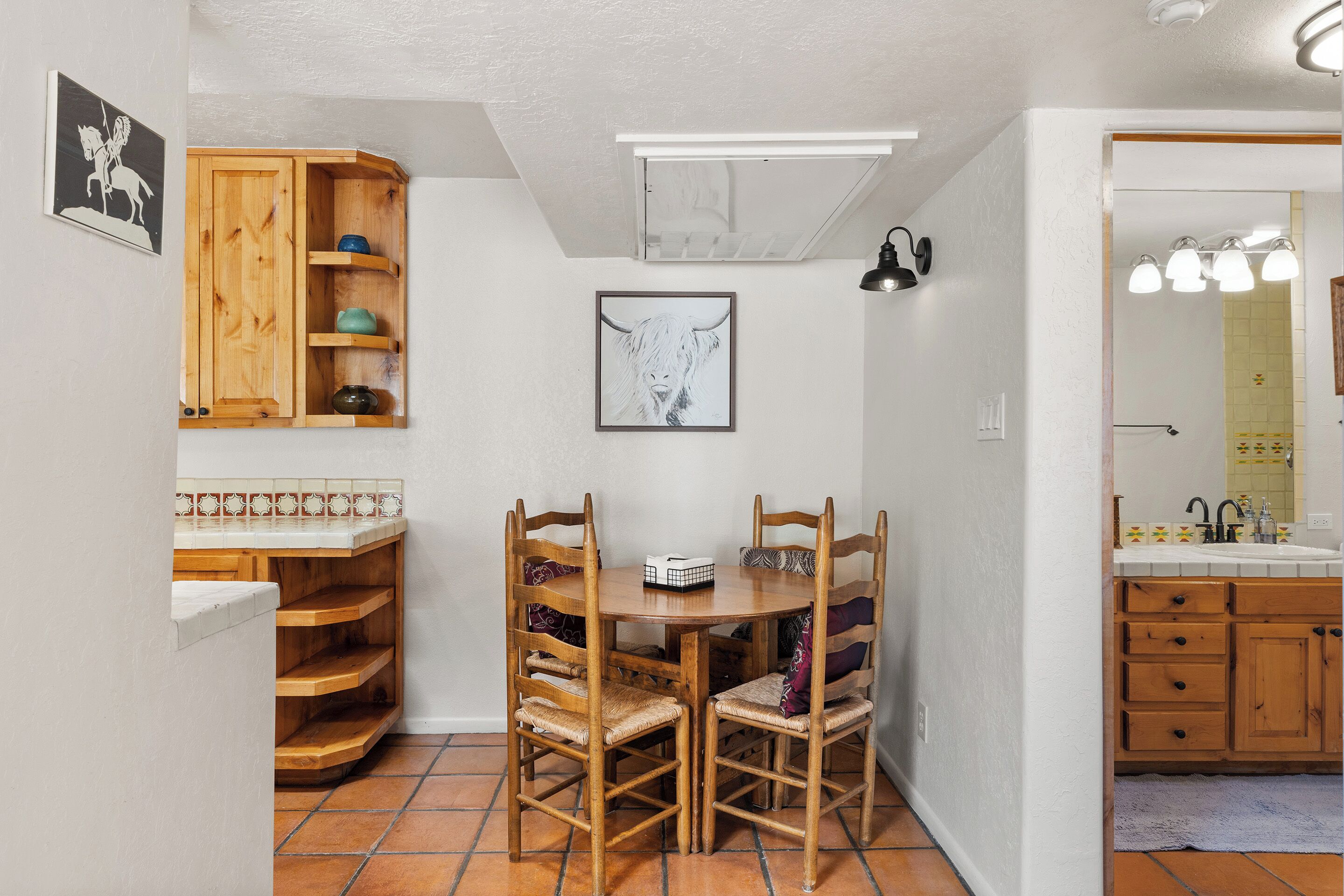 A compact kitchen with wooden cabinets, a dining table with chairs, and a tiled backsplash.