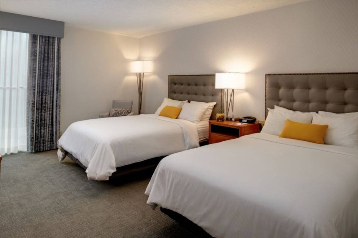 Une chambre d’hôtel avec deux lits, chacun doté d’une tête de lit, de tables de chevet, de lampes et d’une fenêtre avec des rideaux.