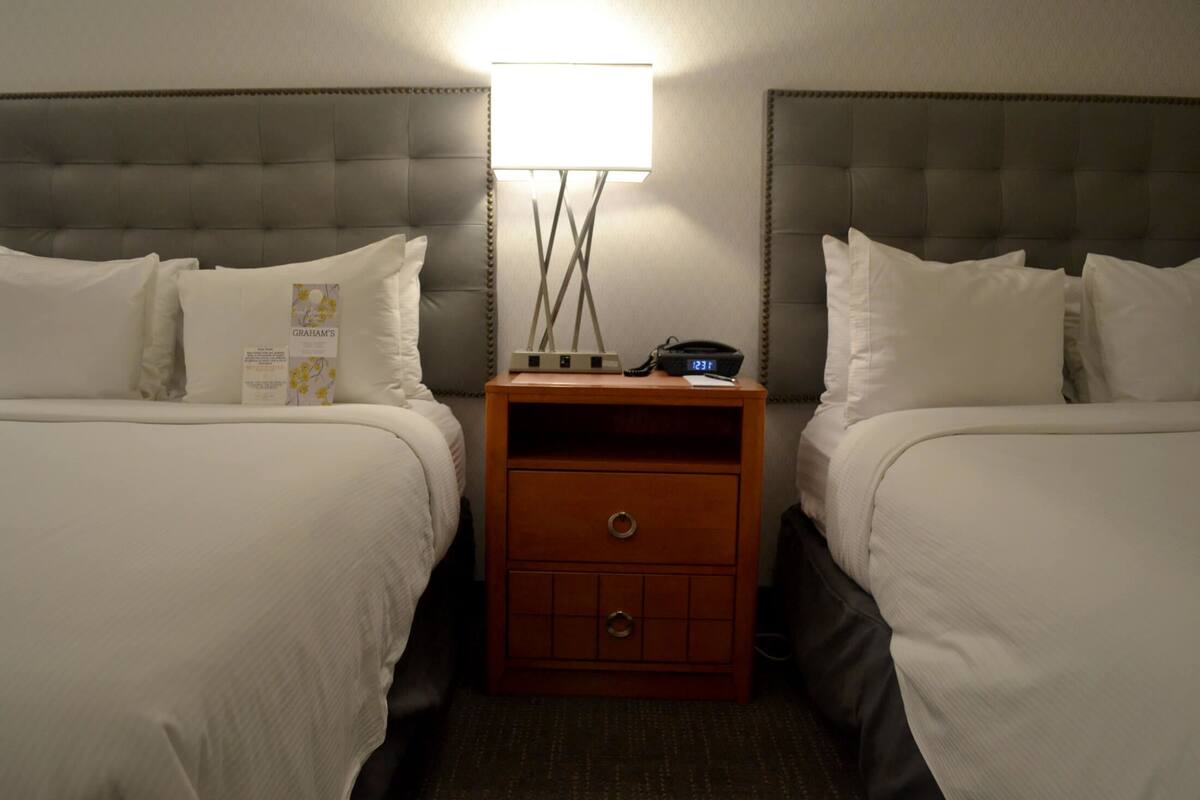 Une chambre d’hôtel avec deux lits, une table de chevet avec une lampe et une horloge.