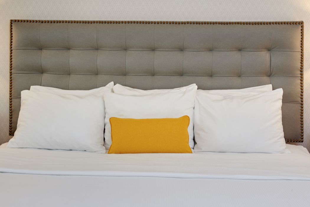 Un letto con testiera capitonata, biancheria da letto bianca e un solo cuscino color senape.