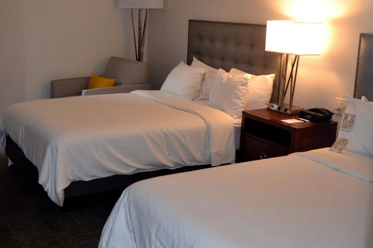 Une chambre d’hôtel avec deux lits, une table de chevet, une lampe et une chaise.