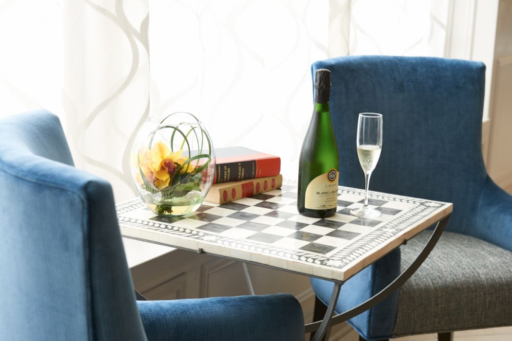 A table with a checkered tablecloth, a bottle of wine, a glass of wine, a vase with flowers, and books.