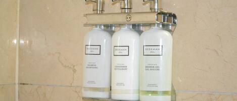 A bathroom with a marble wall and a shelf holding three bottles of Beekman products.